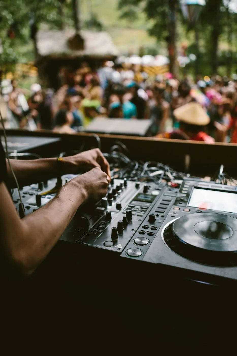A DJ playing an outdoor party in the daytime, crowd in the sun.